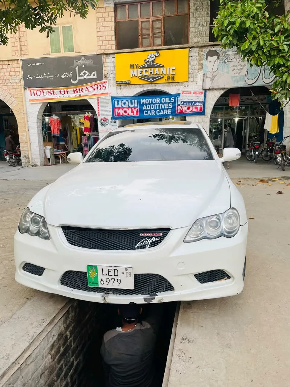 White Toyota Mark X over the service pit with a mechanic working underneath