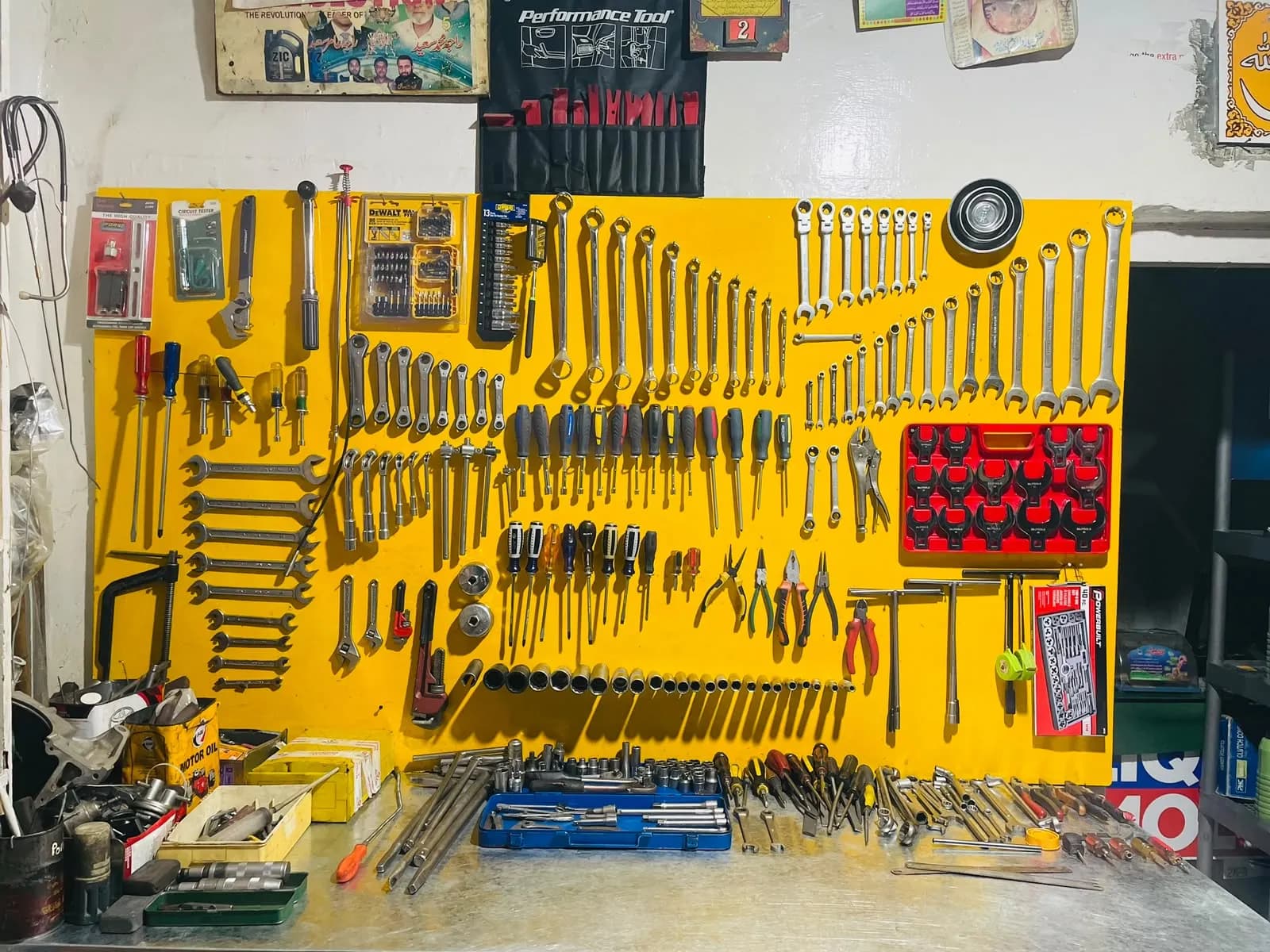 Workshop wall of spanners, screwdrivers, pliers and socket sets neatly arranged on yellow pegboard above a workbench